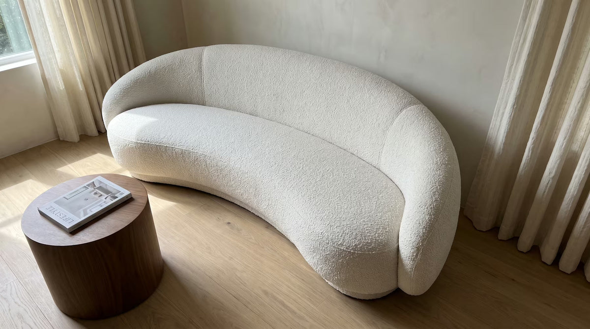 White bouclé curved sofa beside a round walnut side table