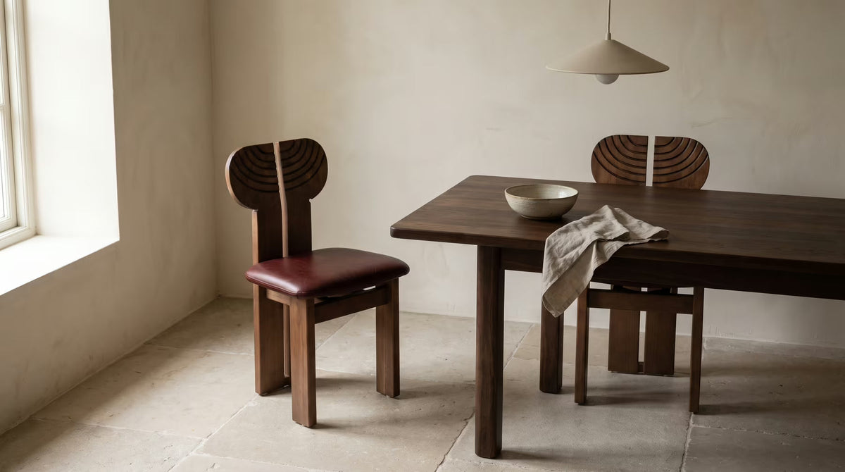 Carved-back wooden dining chairs with oxblood seats beside a dark table