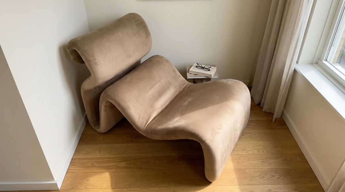 Tan velvet serpentine chaise in an alcove with open floor beside it