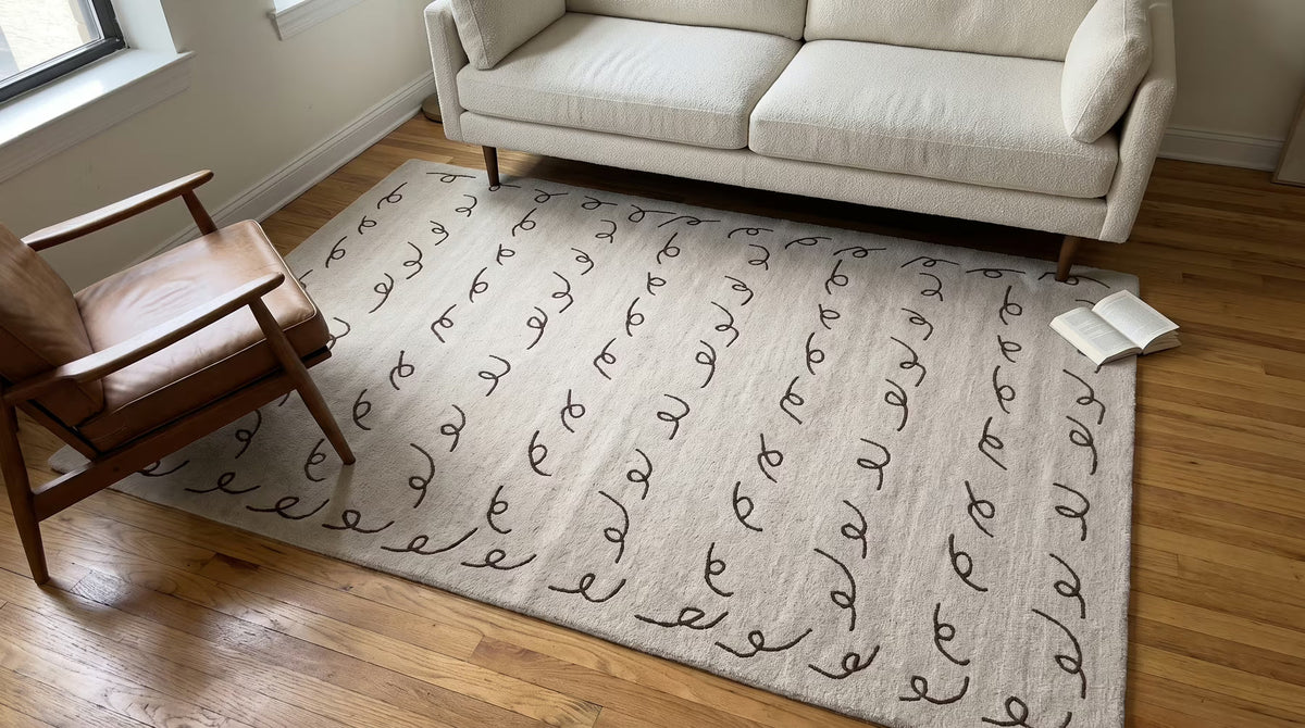 Beige patterned wool rug beneath a sofa and wooden lounge chair
