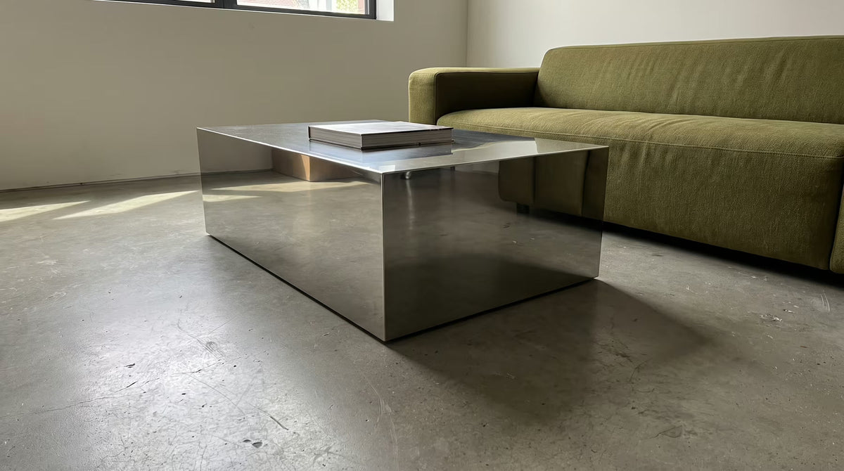 Low stainless-steel coffee table beside an olive sofa